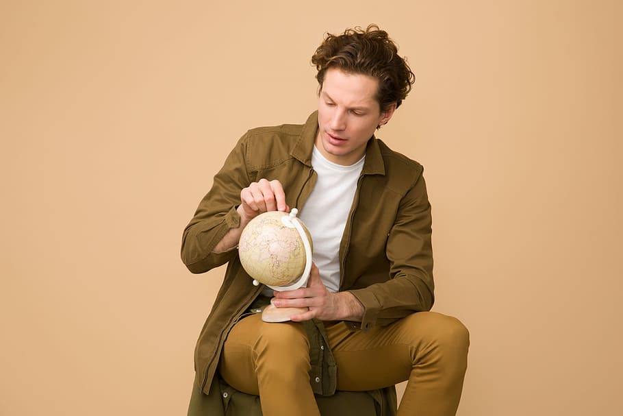 man holding globe while on sit, man sitting on chair holding brown table globe