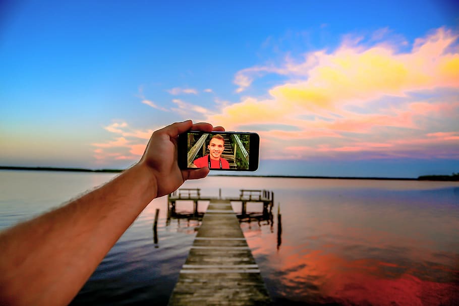 man taking selfie on dock, arm, beach, blur, camera, cellphone