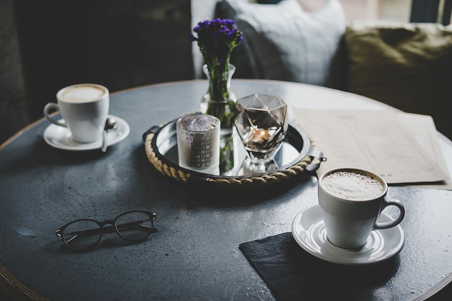 round tray with flower vase between two white ceramic teacups above table, two white ceramic cups on saucers HD wallpaper
