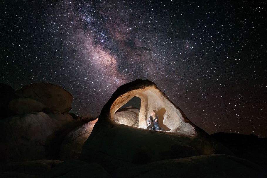 man inside a cave, person sitting on rock formation under starry sky HD wallpaper