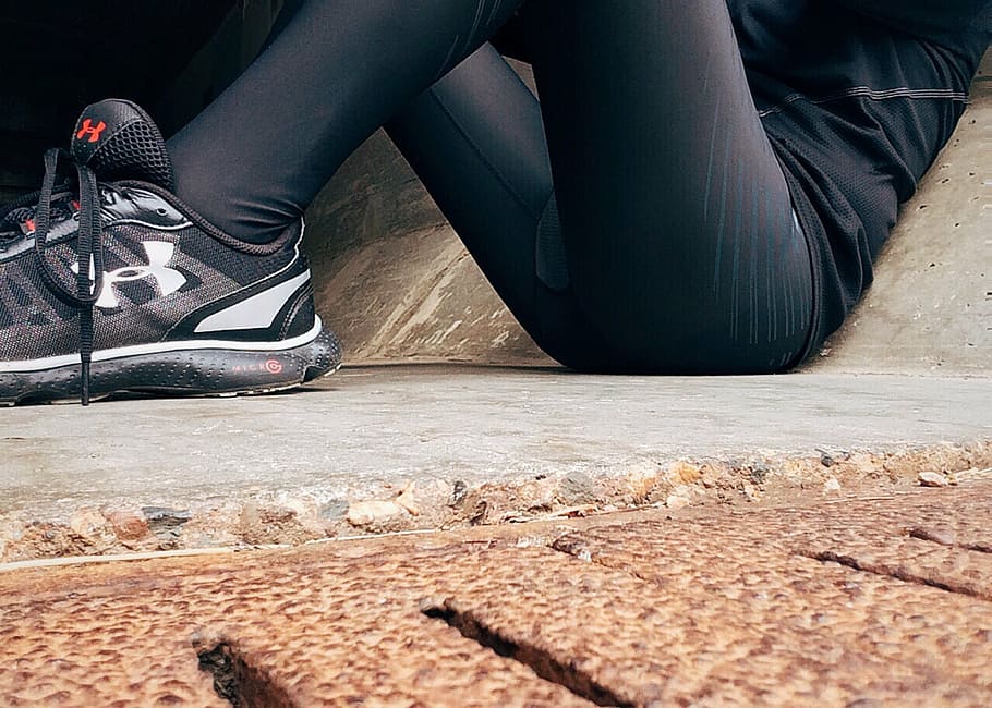 person wearing gray Under Armour running shoes laying on floor while leaning on concrete wall, HD wallpaper