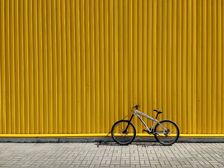 gray and black bike leaning on wall, bicycle leaning on yellow intermodal container