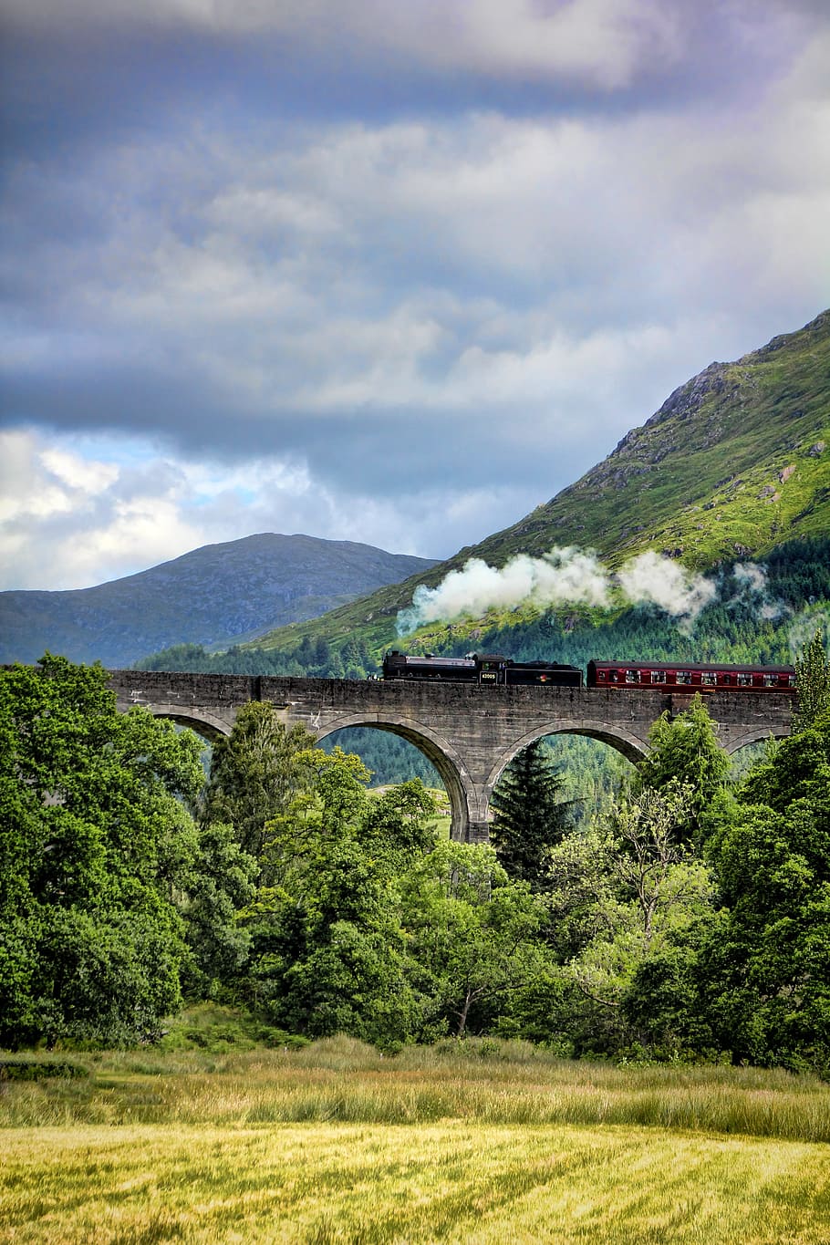 landscape photo of mountains near bridge, train, hogwarts, scotland