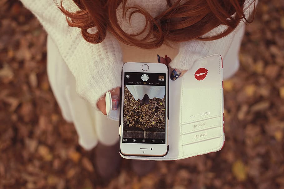 shallow focus photography of woman in white sweater holding gold iPhone 6 showing camera interface