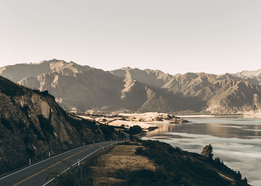 road at the foot of the mountain near lake, landscape photography of asphalt road beside mountain HD wallpaper
