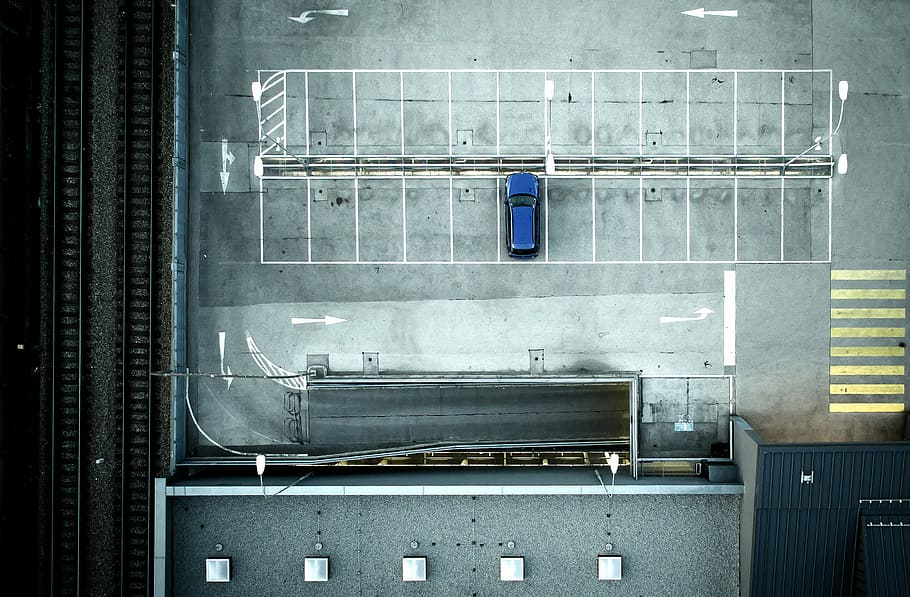 red car parked beside train rail, aerial view of blue car parked on parking lot