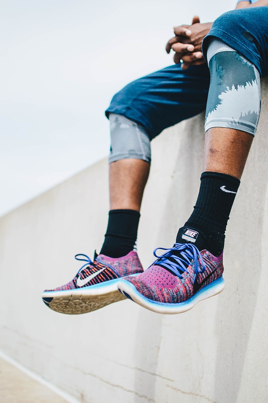 man sitting on the edge of a concrete building wearing Nike running shoes during day, photo of person sitting and wearing purple Nike shoes and black sock, HD wallpaper
