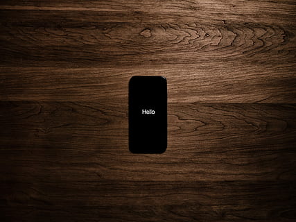 iPhone on wooden surface, turned on iPhone displaying Hello on brown surface HD wallpaper