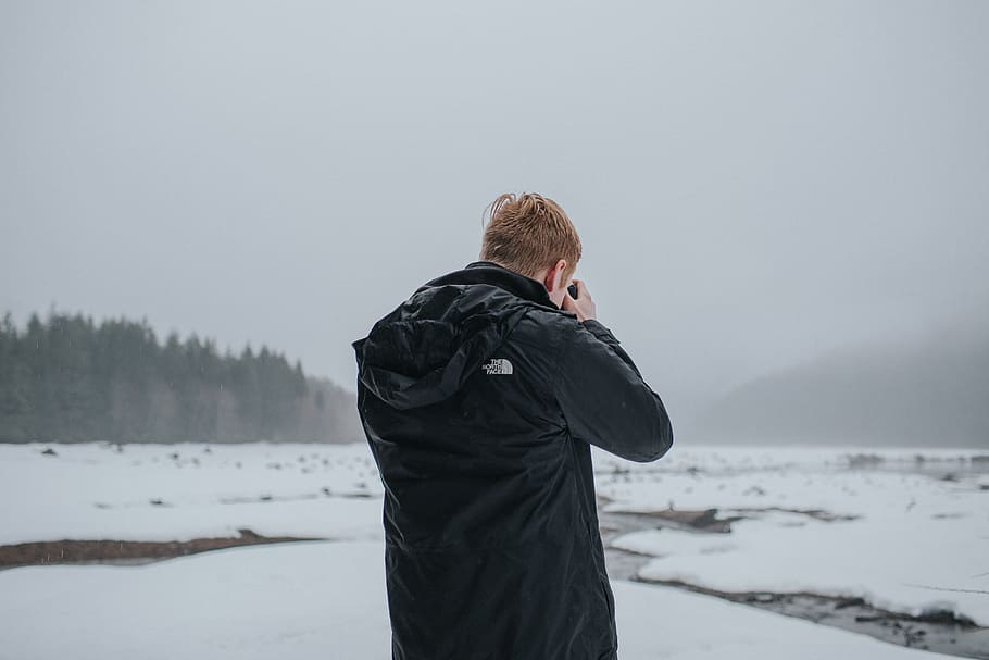 man taking picture under cloudy sky, man wearing black jacket while taking photos on icy field HD wallpaper