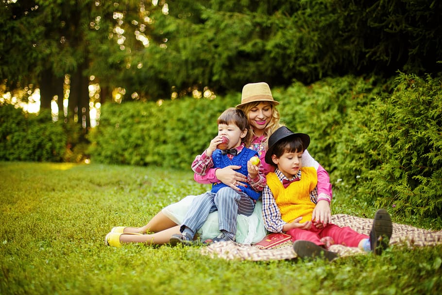 woman hugging her two kids on picnic mat, park, mom and sons