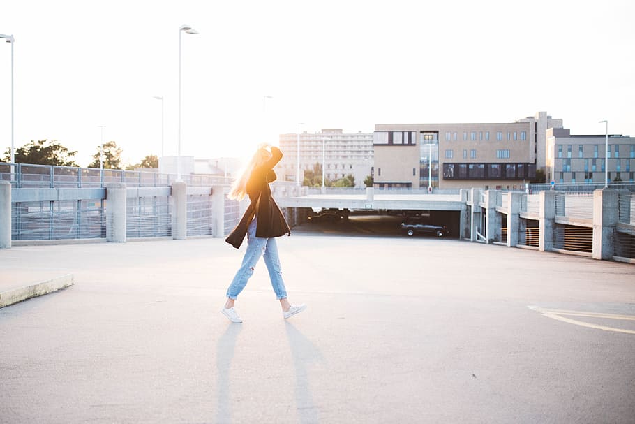 woman walking on road near building at daytime, woman in black top walking near beige building