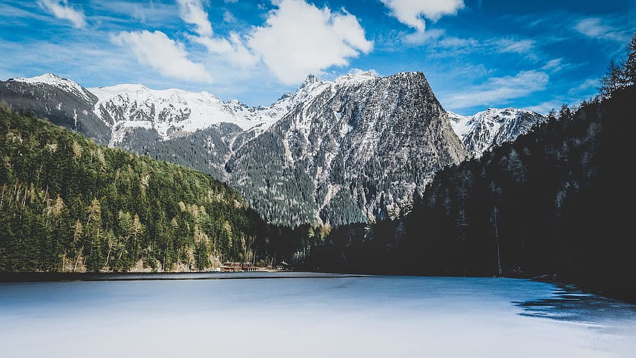 gray mountain covered with snow during daytime, lake surrounded by trees near snow-covered mountain during daytime HD wallpaper