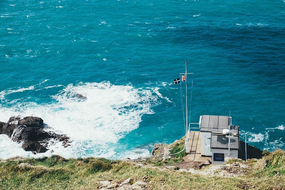 Cape Cornwall, gray building with flags near ocean at daytime HD wallpaper