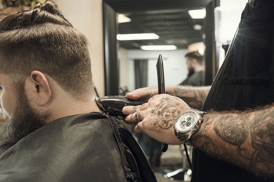person using hair clipper to cut man's hair, man clipping hair beside mirror