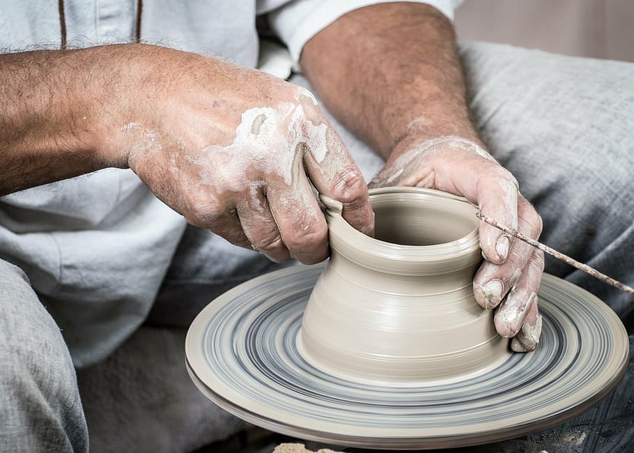 person in gray shirt and gray pants molding clay pot, potter