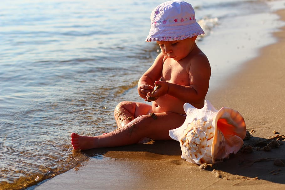baby wearing white hat beside conch shell, kids, sea, beach, happy