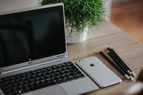 Silver Acer laptop on a wooden desk with a green plant, pencils and an Apple iPhone HD wallpaper