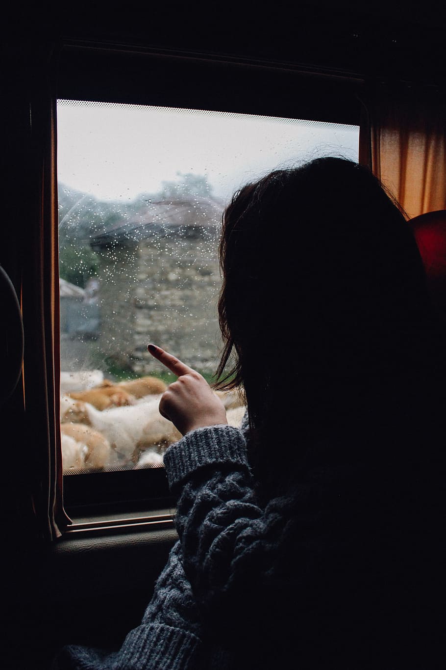 woman in gray knitted sweater looking and pointing at the window, woman pointing her finger on glass window