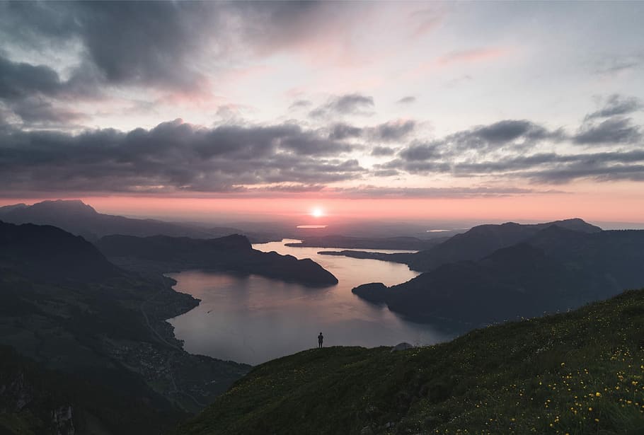 silhouette of person standing on lake surrounded by mountains under cloudy sky during golden hour, aerial view of lake surrounded by mountains HD wallpaper