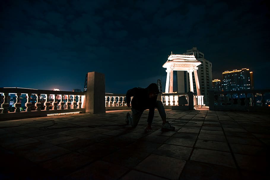 person in black outfit kneeling near concrete bench, person making tricks on terrace during night time HD wallpaper