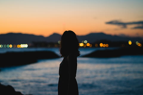 silhouette of woman standing beside body of water, silhouette photo of a woman standing near body of water under cloudy sky during golden hour HD wallpaper