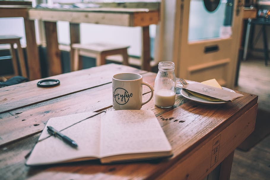 white book behind mug, black click pen on open diary beside white ceramic mug HD wallpaper