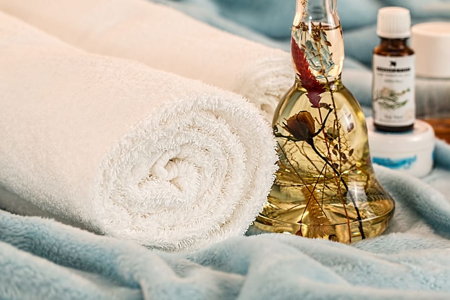 rolled bath towel beside brown liquid filled bottle, massage therapy