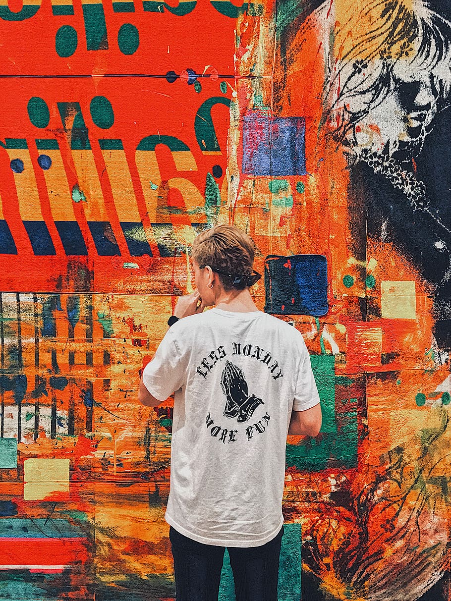 man holding his chin facing multicolored painted wall, photo of man wearing shirt doing artwork on wall