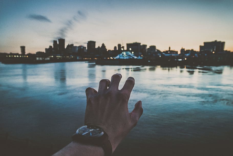 person's left hand reaching city scapes photography, illusion of person grabbing cityscape while wearing black analog watch HD wallpaper