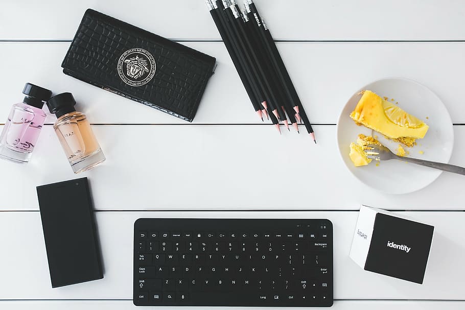 black wireless keyboard; plate with spoon; pencils; Versace wallet; two clear glass bottles HD wallpaper