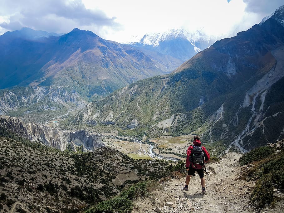 person in red top waling beside mountain, man standing on top of rocky cliff facing green filled mountains HD wallpaper