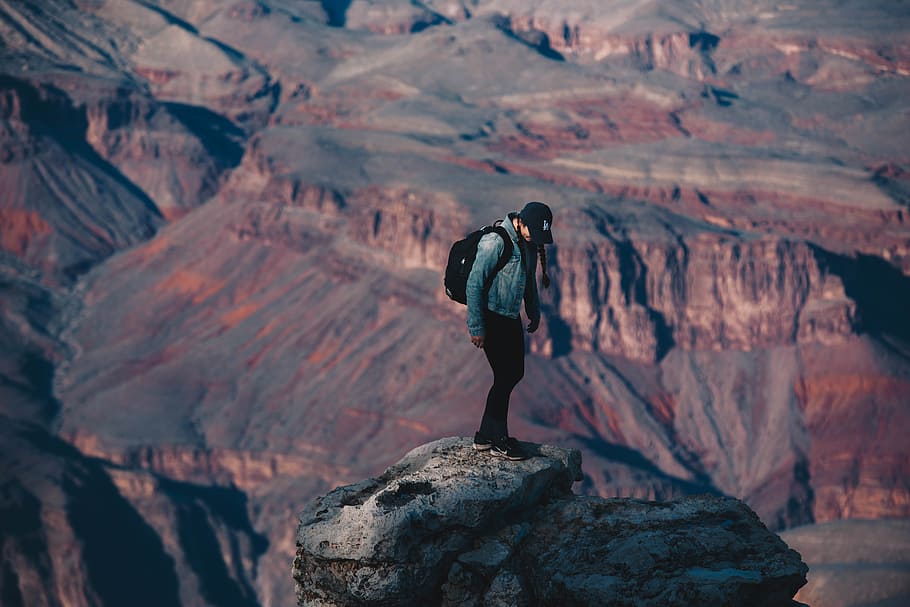 man standing on rock cliff overlooking canyon during daytime, man standing on cliff during daytime, HD wallpaper