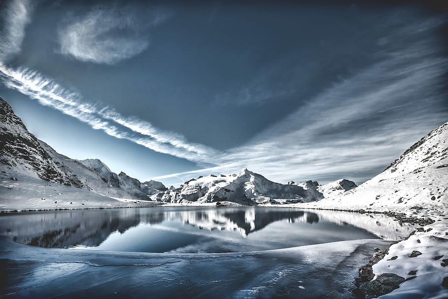 body of water between mountain range covered in snow under gray sky and white clouds at daytime, snow covered with snow under clear sky during daytime HD wallpaper