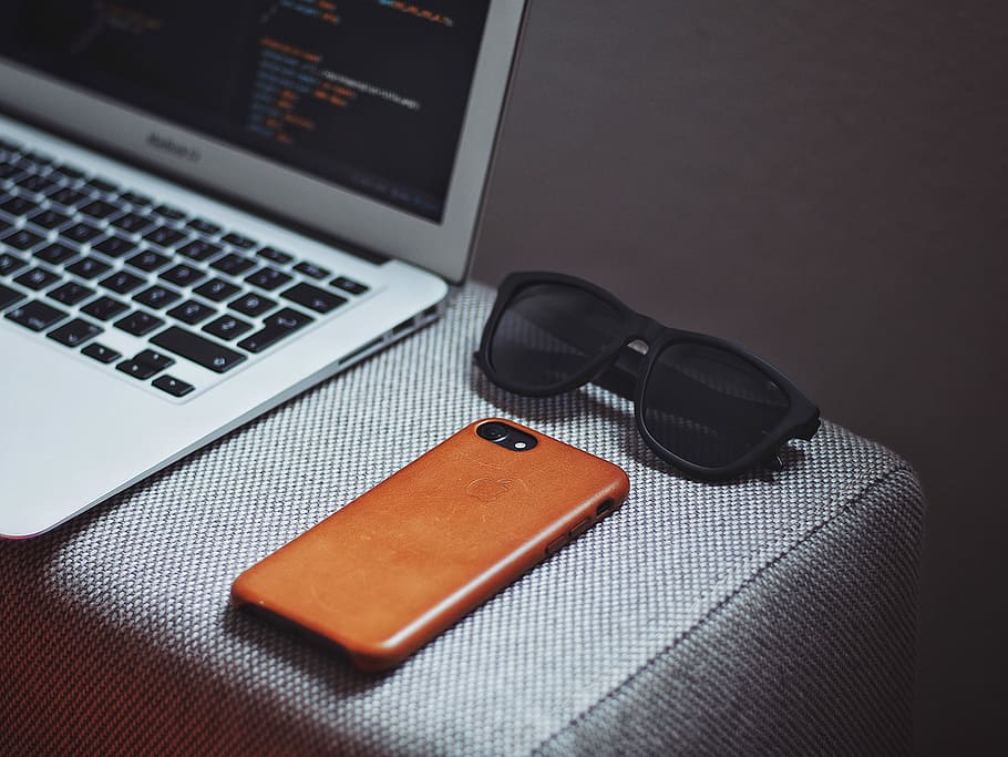 orange smartphone near black framed sunglasses beside MacBook Air, black framed sunglasses near iPhone HD wallpaper