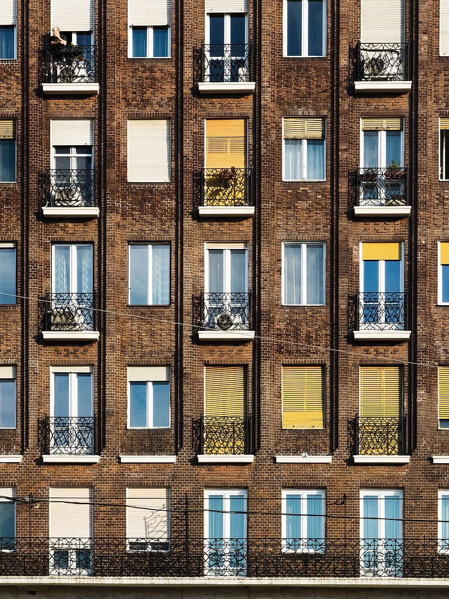 brown concrete apartment during daytime, person leaning on window HD wallpaper