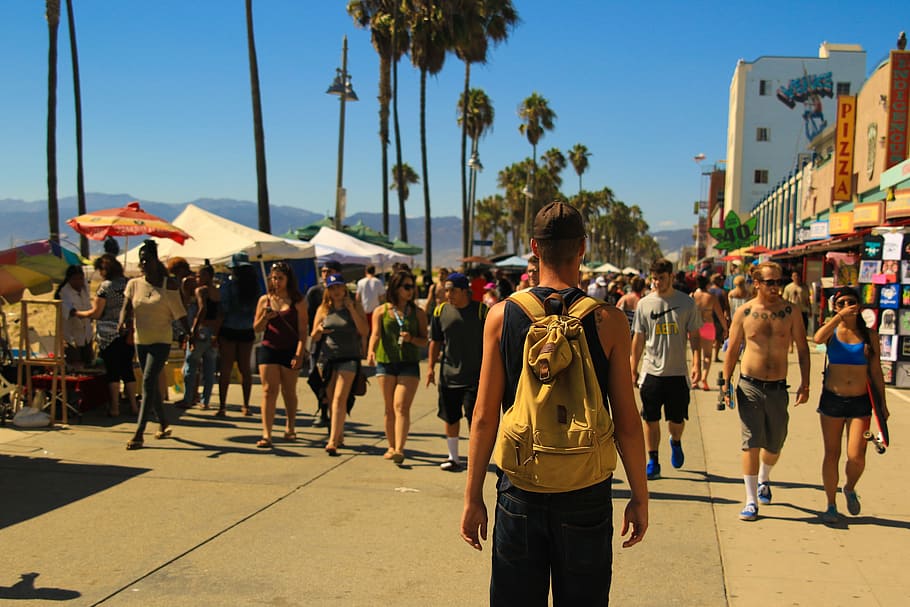 man standing on road, man carrying yellow backpack in front of pathway during daytime HD wallpaper