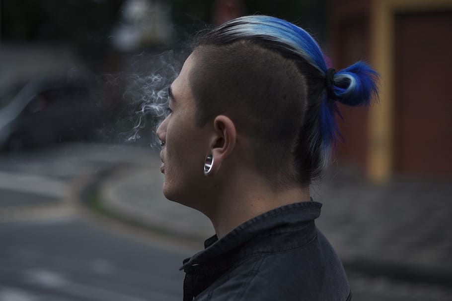 selective focus photography of man with blue mohawk hair, man wearing black collared top