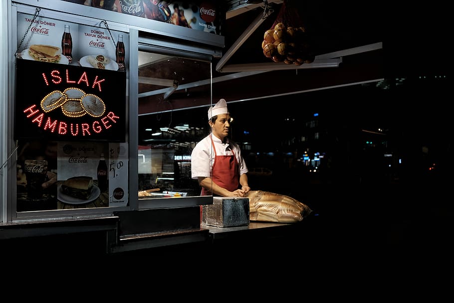 man standing on hamburger stall during night time, chef standing in gray food kiosk during nighttime