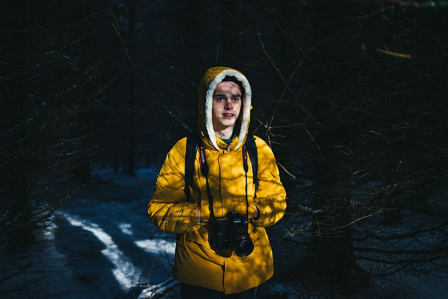 man wearing parka jacket and surrounded by trees, man in yellow hoodie carrying black DSLR camera HD wallpaper