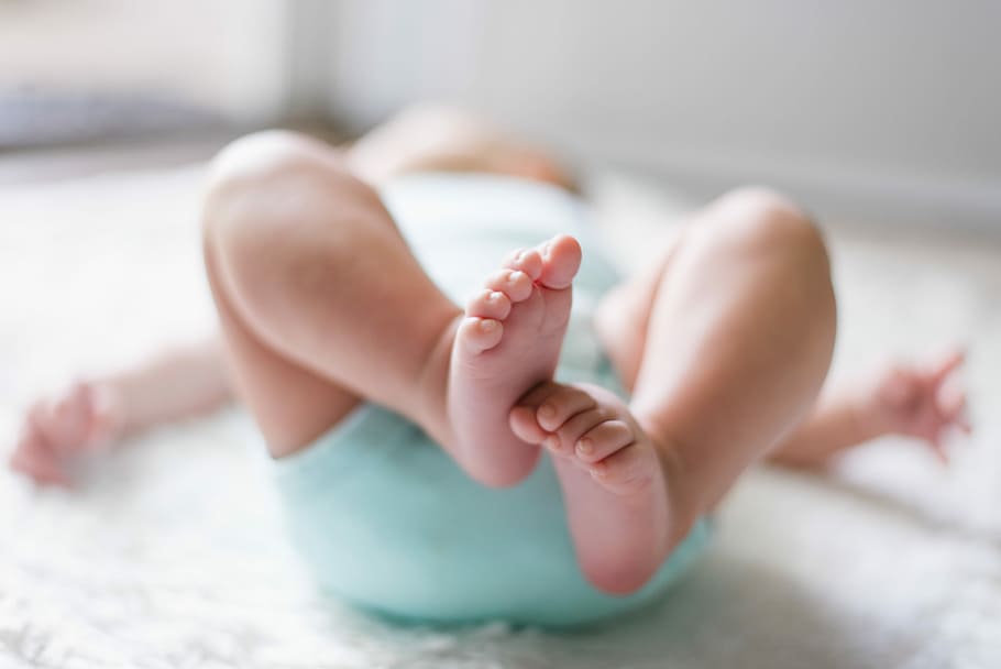 baby laying on bed, baby wearing teal onesie, feet, legs, toes