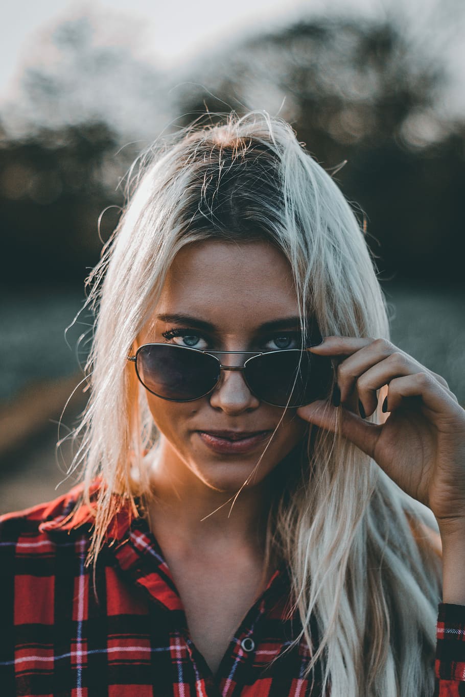 woman wearing red and black plaid top holding sunglasses, woman holding her sunglasses in selective focus photography