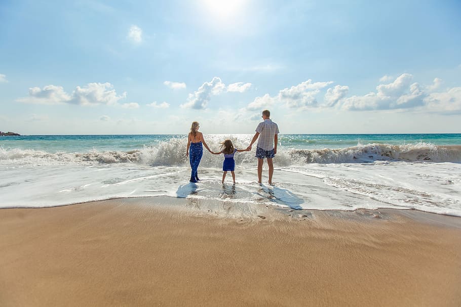 man, woman and child holding hands on seashore, girl in between man and woman holding hands standing on seashore