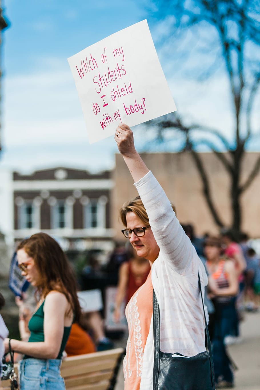woman holding white paper, woman in white cardigan and pink shirt walking on street while holding paper board with text HD wallpaper