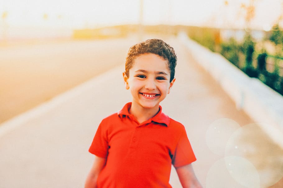 smiling boy wearing red polo shirt, boy wearing red polo shirt standing near pavement HD wallpaper
