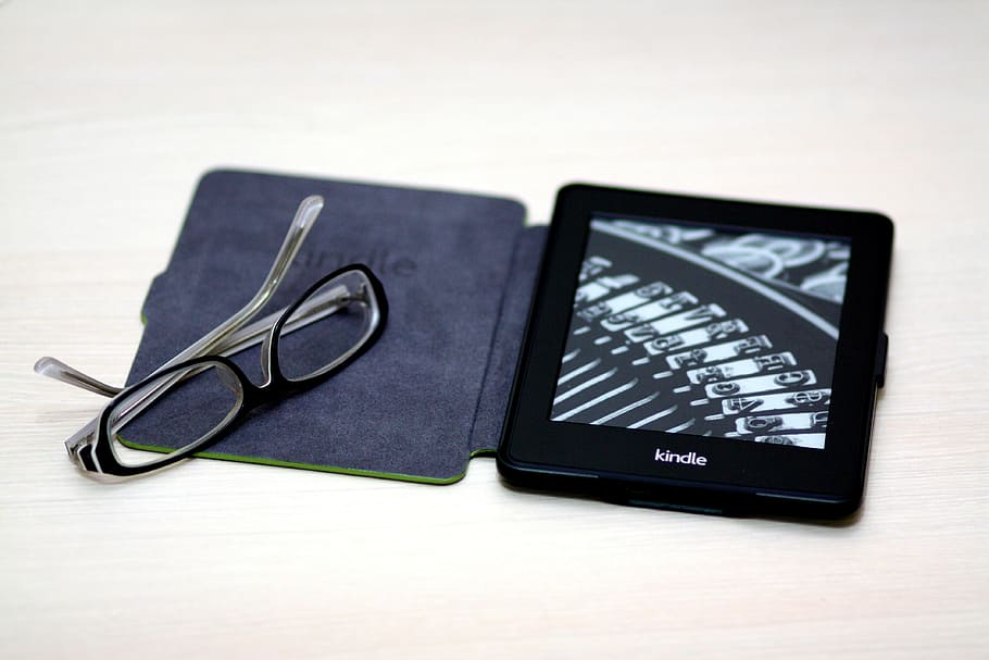 black Amazon Kindle e-book reader on brown surface near black framed eyeglasses, HD wallpaper
