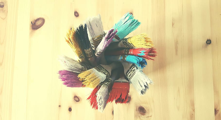 macro shot of assorted paint brushes placed on clear glass container on brown wooden surface