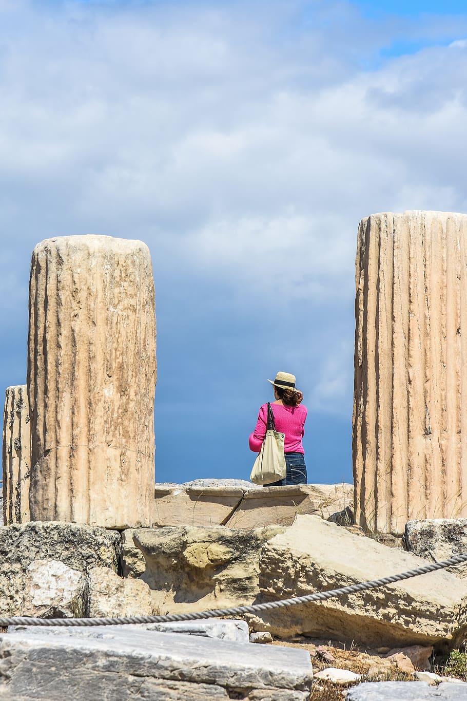 woman standing between concrete pillars under white clouds and blue sky at daytime HD wallpaper
