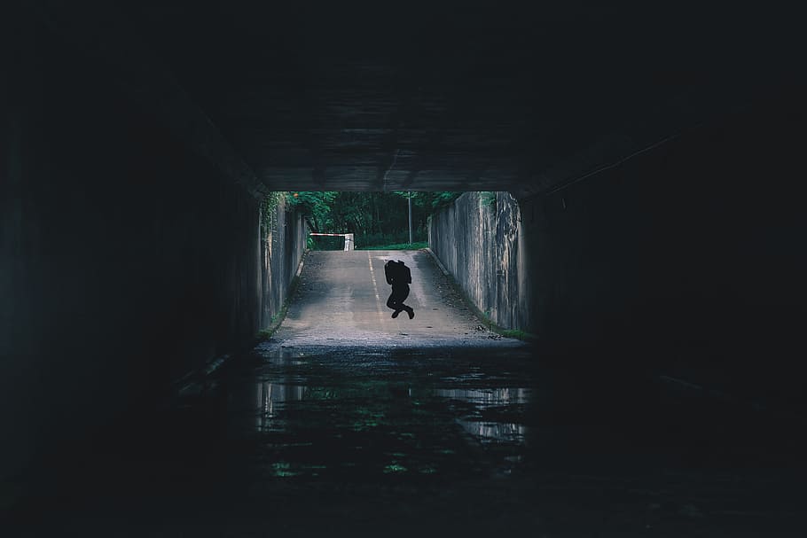 silhouette of person inside tunnel, silhouette of person jumping on gray asphalt road during daytime