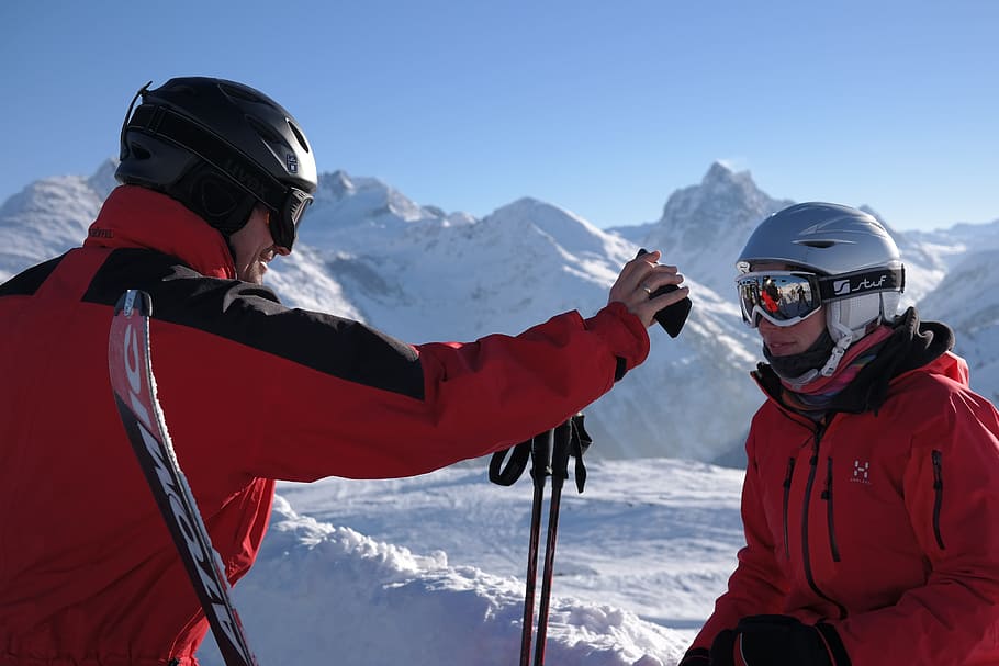 man holding phone standing beside woman wearing gray helmet, Skier