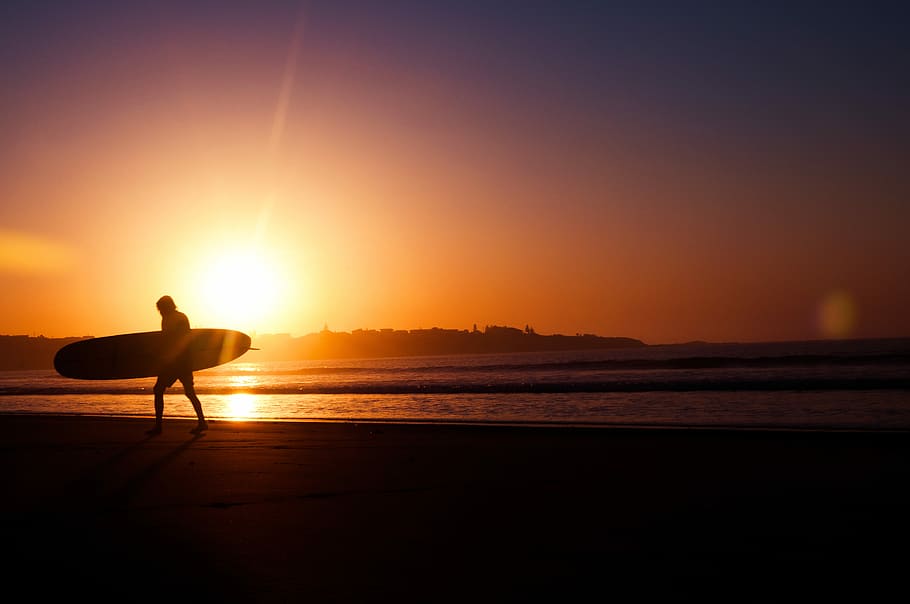 silhouette of man holding surfboard near seashore during sunset, person holding surfboard near seashore HD wallpaper